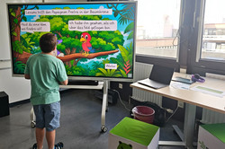 Junge steht vor dem Smartboard und löst das Leserätsel