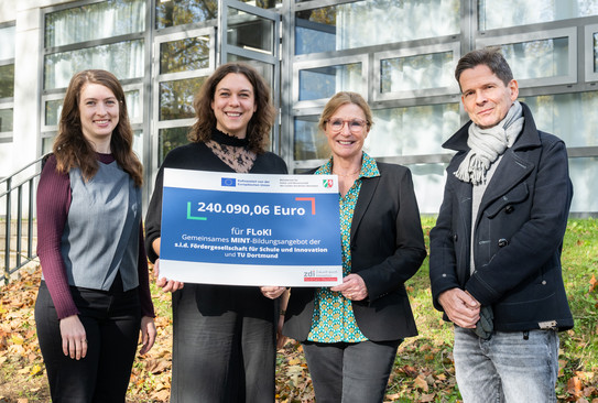 Vier Mitglieder des FLoKI-Projektteams stehen vor einer Glasfassade und präsentieren gemeinsam einen Förderbescheid über 240.090,06 Euro. Der Bescheid informiert über die Förderung des gemeinsamen MINT-Bildungsangebots von KITZ.do und TU Dortmund.