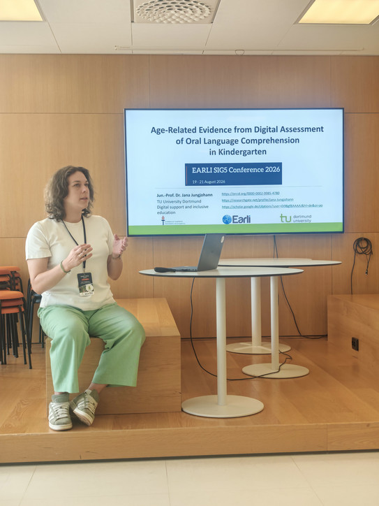 Foto von Jun-.Prof. Dr. Jana Jungjohann in sitzender Position vor der ersten Vortragsfolie mit dem Vortragstitel Age-Related Evidence from Digital Assessment of Oral Language Comprehension in Kindergarten auf der ERALI SIG 5 2026 in Jyväskylä